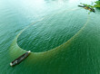 © AmazingAerialAgency - Aerial view of fishermen in wooden boats casting a large circular fishing net on the green waters of Kaptai Lake Rangamati, Chittagong Division, Bangladesh.