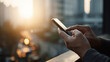 © Bangmunce - Hands Scrolling Smartphone with Golden Sun Flare and Cityscape