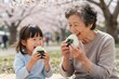 © Rixar - Japanese grandmother and granddaughter laughing eating onigiri during picnic