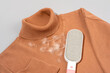 © Garnar - Reusable lint remover brush removing pet hair and lint from brown knit turtleneck sweater on light gray background. Concept of gentle fabric care for wool garments, allergy control, clothing cleaning