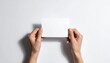 © ruangrit19 - Top view of two hands holding a blank white rectangular card against a clean background perfect for mockup design and promotional messaging.