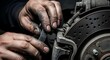 © Tarring - Close-up of a mechanic's dirty hands working on a car's disc brake system with a wrench, performing maintenance or repair.