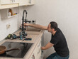 © Михаил Решетников - A plumber is replacing a faucet in the kitchen.