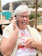 © luciano - Happy Senior Woman Laughing On Phone At Outdoor Beach Cafe During Sunny Vacation