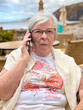 © luciano - Elderly Woman Talking On Phone At Seaside Cafe In Casual Summer Clothing