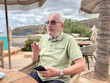 © luciano - Elderly Man Conversing at Beachside Cafe Holding Smartphone Relaxed Senior on Coastal Vacation