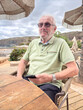 © luciano - Senior Man Relaxing at Beachside Café With Smartphone During Coastal Vacation and Leisure Time