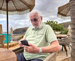 © luciano - Senior Man Using Smartphone at Beachside Cafe During Overcast Seaside Vacation