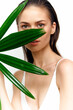 © VICHIZH - A young woman partially obscured by a large green leaf, showcasing natural beauty and a serene expression for lifestyle or beauty projects.