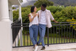 © wavebreak3 - Diverse couple standing on balcony, holding clear drinking glass and leaning on black railing