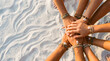 © Mubarak - A group of diverse hands stacked together on soft white sand, symbolizing unity and teamwork.