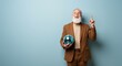 © Ryzhkov - Joyful elderly man in a brown suit holding a blue disco ball and pointing upward against a blue background for lifestyle marketing, party planning and creative advertising