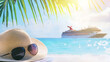 © Ruslan - A straw hat and sunglasses on a tropical beach with palm leaves and a cruise ship in the background – summer accessories, vacation concept