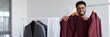 © Iryna - Man holding multiple burgundy suits on rack in boutique