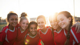 Group of diverse young girls soccer players embracing, celebrating teamwork and success with cheerful expressions during golden hour