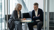 © illustratica - Two European executives discuss business documents in a modern office meeting room