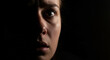 © hadid - Intense gaze of a woman peering from the darkness, her wide eye reflecting profound fear and a moment of sudden surprise or emotional distress in a suspenseful setting