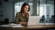 © twilight mist - Professional woman smiling while working on her laptop in a modern office environment.