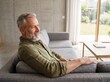 © Giama22 - Serene mature man with a groomed beard, wearing a casual green shirt, relaxing on a couch in a minimalist modern home, 50-year-old male portrait.