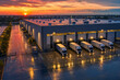 © angelmaxmixam - Aerial view of a modern logistics warehouse with numerous semi trucks backed into loading docks at a vibrant, colorful sunset. Busy distribution center operations.