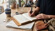 © velikiyzayats - Young man planning travel itinerary in notebook at cafe table with map and compass