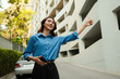 © Parichat - Young Asian woman hailing ride with smartphone in city