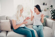 © deagreez - Mother and adult daughter arguing on a couch in a living room, emotional family conflict and tense conversation between two women