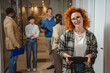 © Miljan Živković - Redhead woman holding clipboard smiling in office hallway