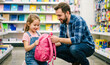 © Taras Roshchuk - A father and his young daughter stand in a store aisle filled with school supplies. The girl smiles as her father shows her a pink backpack. They are happy together while shopping