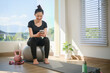 © wattana - Young woman sitting on a fitness ball, checking her smartphone after a home workout in a bright and modern living space.