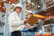 © AU USAnakul - Two Caucasian men are meticulously examining metal sheets and cardboard box within warehouse environment, engaged in focused discussion with serious expression while inspecting production materials.