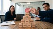 © Muhammad Usman - Business Team Collaborating as Hand Places Target on Wooden Block Pyramid