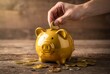 © MohammadIshak - Hand depositing coin into a yellow piggy bank on a wooden table