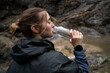 © Соня Монштейн - Side view portrait of young Caucasian woman traveler drinking water outdoors while hiking in the mountains.