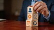 © Emma - Business man stacking wooden blocks with icons representing human resources settings checklist calendar and recycling symbols concept of management strategy teamwork and