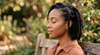 © Shiv - Black woman meditating outdoors with eyes closed on a wooden bench surrounded by greenery african american hair braids