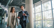 © Gorodenkoff - Two Focused Business Professionals Walk Through a Bright Office Atrium Reviewing a Digital Tablet, Checking Project Status, Adjusting Priorities, Confirming Deadlines, and Coordinating Next Actions