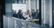 © Gorodenkoff - Business Leaders Sit Around a Conference Table Reviewing Charts on a Large Screen, Debating Results, Setting Priorities, and Planning Next Steps While Using Laptops, Printed Reports, and Notes During