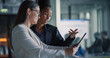 © Gorodenkoff - Female Business Professionals Stand in a Modern Office Hallway Reviewing a Digital Tablet, Updating Sales Pipelines, Refining Customer Journeys, Planning Product Launches, and Aligning Revenue Target.