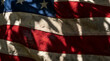 © solavie - A weathered national flag, textured by time, draped with dramatic sunlight and casting intricate leaf shadows, symbolizing strength, endurance, and profound heritage