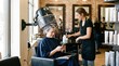 © DenS - Woman sitting under hair dryer in salon getting styled by attendant