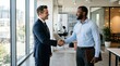 © salam - Two businessmen shaking hands in a modern office hallway with large windows.