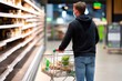 © Kingboy - Shopper in Mask Pushing Overloaded Cart in Grocery Store Aisle with Shelves in Background