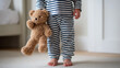 © photo for everything - Toddler in striped pajamas with teddy bear, barefoot on carpet, a candid moment of childhood innocence and comfort, perfect for home settings