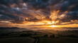 © Tyo - Golden sunbeams burst through dramatic clouds over rolling hills at sunrise