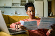 © Marko Geber - Concerned woman reviewing household bills at home with laptop