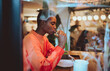 © BullRun - Cheerful woman browsing her mobile device in a modern eatery, combining digital communication with a lunch break, highlighting 5G technology and the lifestyle of a contemporary professional.