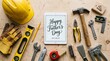 © zephyr - Tablet computer displaying happy fathers day greeting surrounded by a collection of construction tools and safety equipment on a rustic wooden table top background surface