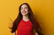 © SHOTPRIME STUDIO - Young woman with long hair and closed eyes smiling happily against yellow background. Female in red shirt enjoying positive emotions with natural beauty and relaxed posture.