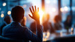 © Kateryna - Cinematic wide back view of a silhouetted figure with a raised hand seated among other silhouettes in a bright softly defocused boardroom seminar raised hand audience question